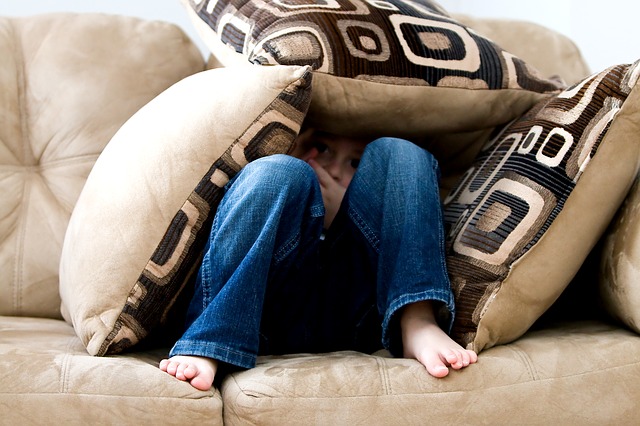 boy with social anxiety disorder hiding under cushions on the couch