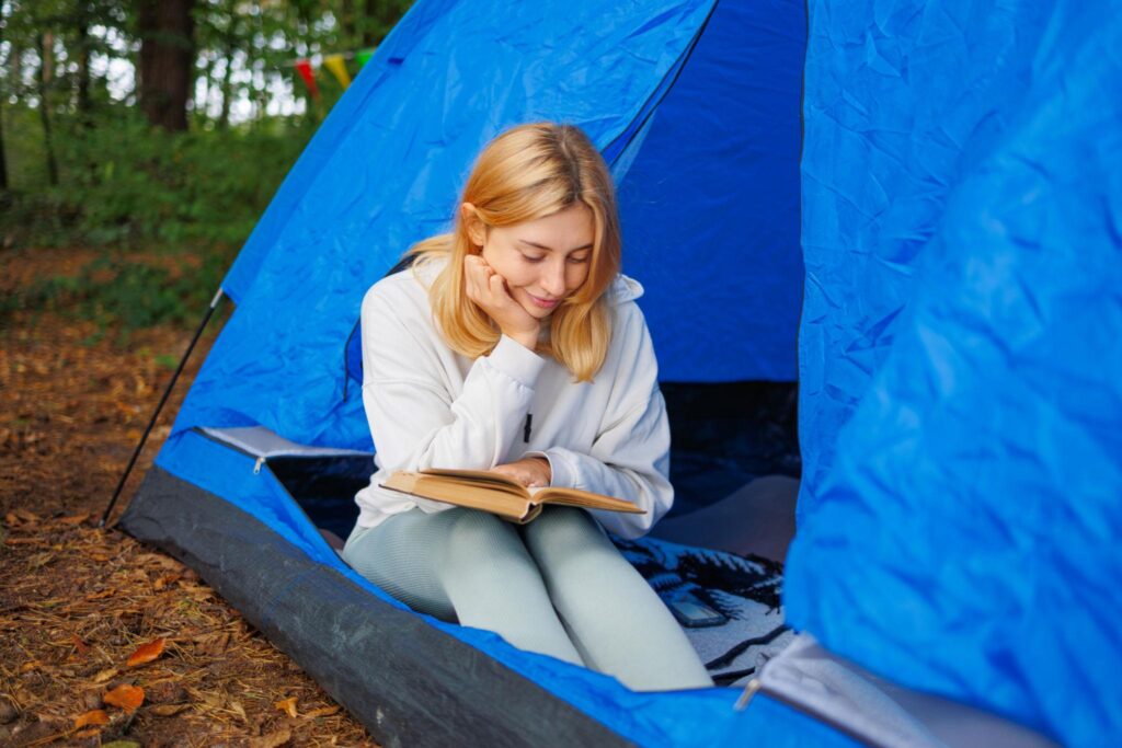 woman reading homeoapthyassoc book while camping